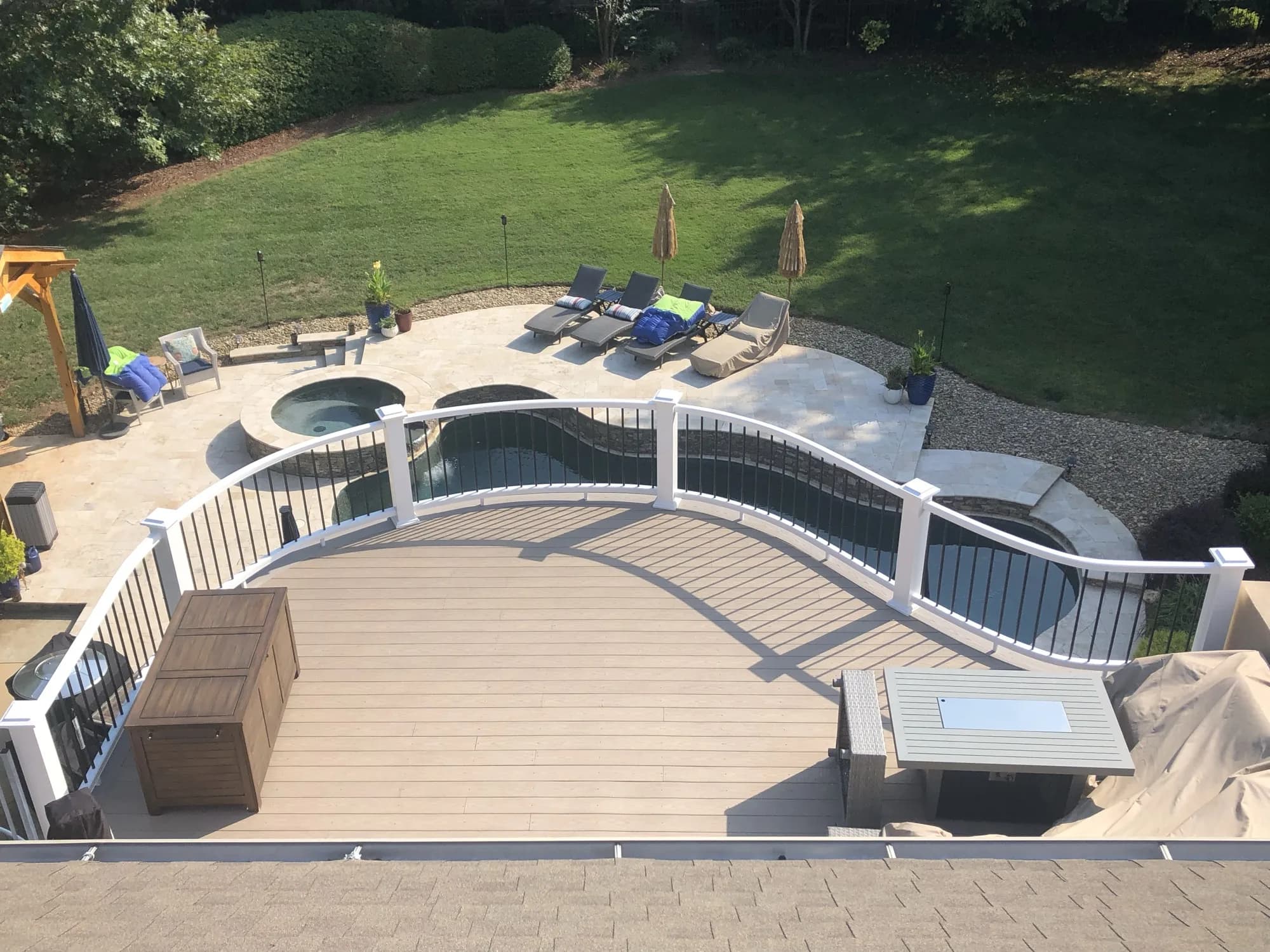 Aerial view of a curved composite deck with a wave-shaped railing overlooking a pool and paver patio in Charlotte, NC